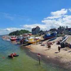 Słoneczny dzień nad polskim morzem. Kolorowe łodzie na plaży, tłumy ludzi, a na wodzie skuter wodny.