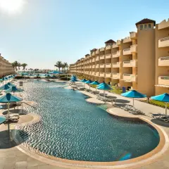 Egipt last minute all inclusive najtaniej: luksusowy basen z leżakami i parasolami, otoczony hotelowymi budynkami. Idealne miejsce na relaks.