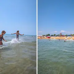 Dwie dziewczynki pluskają się w wodzie na plaży Bibione. W tle widać łódki i parasole.