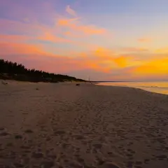 Piękny zachód słońca nad morzem. Niebo mieni się odcieniami różu i pomarańczy, a plaża jest pusta, tylko ślady stóp przypominają o minionych spacerach.