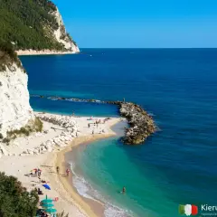 Malownicza plaża nad Adriatykiem z białymi klifami i turkusową wodą. Ludzie odpoczywają na piasku, ciesząc się słońcem.