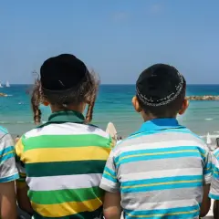 Czterech chłopców w jarmułkach i pasiastych koszulkach patrzy na morze. Wakacje w izrael miasta.