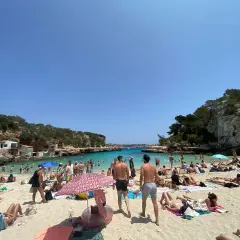 Majorka we wrześniu: słoneczna plaża pełna ludzi, turkusowa woda, skaliste wybrzeże. Idealna pogoda na wakacje.