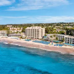Idealne Barbados wakacje: hotel przy plaży z basenami i leżakami, turkusowe morze i zielone wzgórza w tle.