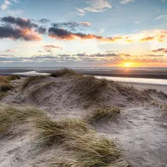 Piękne wydmy i plaża podczas zachodu słońca w Ustce. Słońce maluje niebo na pomarańczowo, a fale delikatnie szumią.
