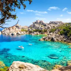 Turkusowa zatoka na Costa Smeralda, z łodziami i skalistymi brzegami porośniętymi zielenią.
