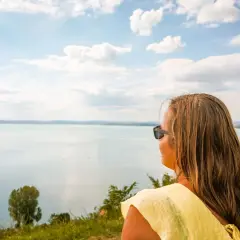 Kobieta w żółtej bluzce podziwia widok na jezioro Balaton podczas wakacji.