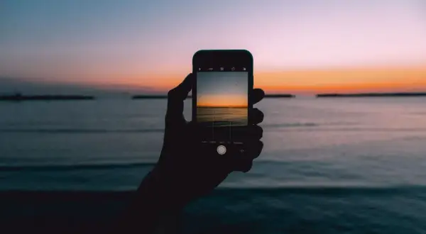 Dłoń trzyma smartfon, na którym widać piękny wschód i zachód słońca nad morzem.