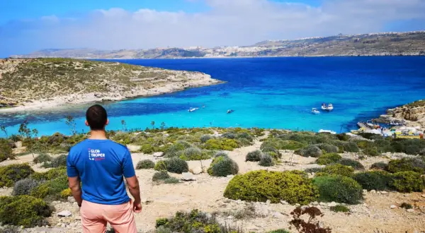 Malta: turkusowa woda, łodzie i skaliste wybrzeże. Widok na zatokę, gdzie widać niewielką ludność korzystającą z uroków wyspy.