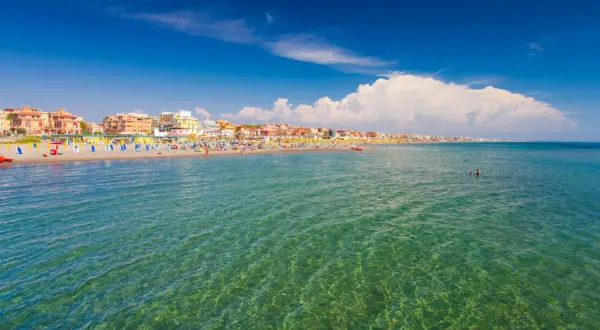 Słoneczny dzień nad morzem w Rzymie. Tłumy plażowiczów, kolorowe parasole i budynki wzdłuż wybrzeża.