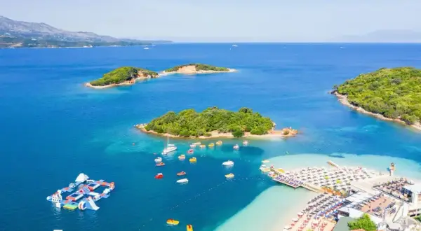 Rajska plaża i wysepki na lazurowym morzu w Albanii. Wodne atrakcje, łodzie i leżaki zapraszają do wypoczynku.