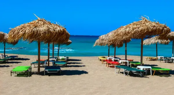 Słomiane parasole i leżaki na piaszczystej plaży Falasarna, z turkusowym morzem w tle.