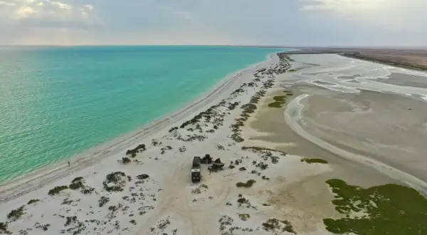 Pustynna plaża z turkusową wodą, gdzie jest Oman. Obóz z samochodami terenowymi i namiotem na piasku.