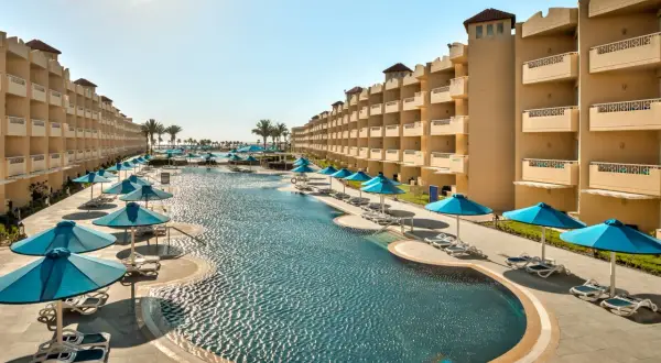 Egipt last minute all inclusive najtaniej: luksusowy basen z leżakami i parasolami, otoczony hotelowymi budynkami. Idealne miejsce na relaks.