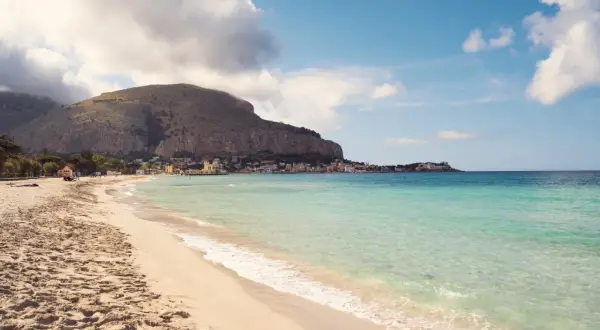 Piękna plaża Mondello z turkusową wodą, piaszczystym brzegiem i malowniczym miasteczkiem w tle.