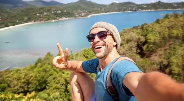 Szczęśliwy mężczyzna robi selfie na tle tropikalnej zatoki. Idealne wakacje dla singli, pełne słońca i przygód.