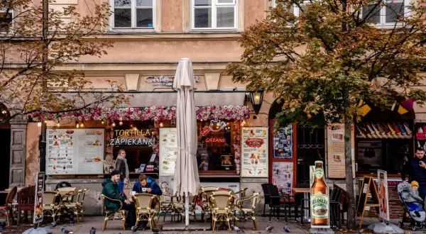 Jesienna Polska na weekend: kawiarnia z zapiekankami i grzanym winem, ludzie siedzą przy stolikach, gołębie spacerują po bruku.