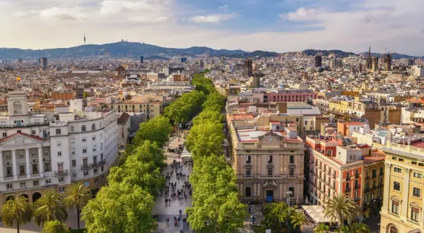 Słoneczna barcelona pogoda listopad. Ludzie spacerują aleją drzew, w tle widać miasto i góry.