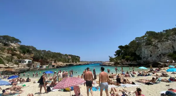 Majorka we wrześniu: słoneczna plaża pełna ludzi, turkusowa woda, skaliste wybrzeże. Idealna pogoda na wakacje.