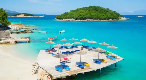 Albania jakie morze? Turkusowa woda, piaszczysta plaża, leżaki i parasole na drewnianym pomoście. Idealne miejsce na wakacje.