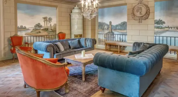 Elegancki salon w hotelu 5 gwiazdkowym. Miękkie sofy, aksamitne fotele i zabytkowy piec tworzą przytulną atmosferę.