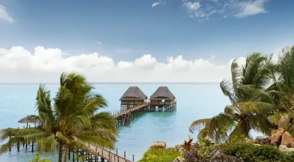Dwa domki na wodzie na Zanzibarze, otoczone palmami. Nawet podczas pory deszczowej Zanzibar zachwyca pięknem.