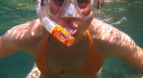 Kobieta w masce i rurce do oddychania, odkrywająca uroki snorkelingu. Woda jest przejrzysta, a światło słoneczne tworzy na jej skórze piękne refleksy.