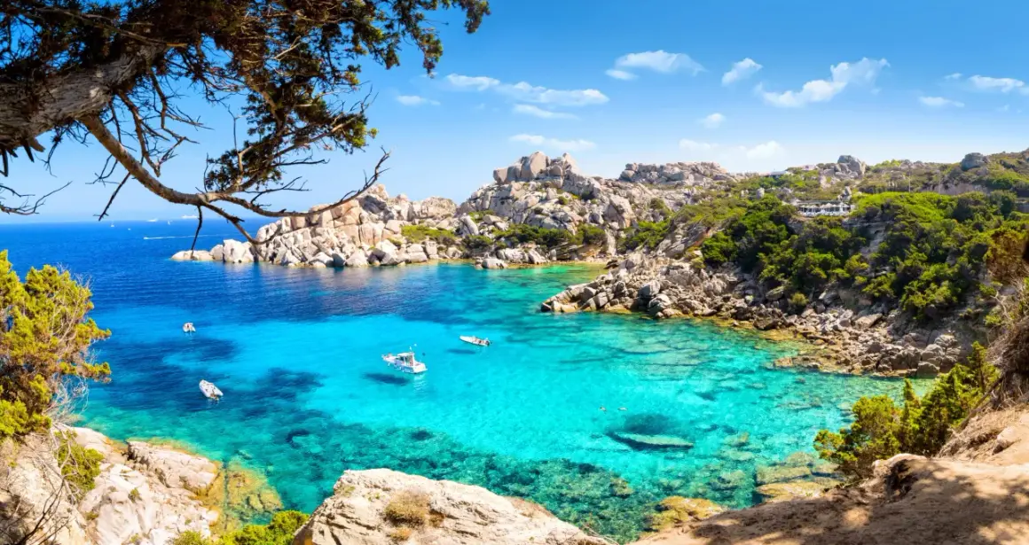 Turkusowa zatoka na Costa Smeralda, z łodziami i skalistymi brzegami porośniętymi zielenią.