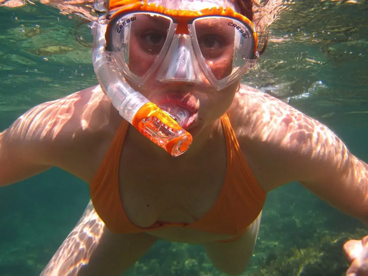 Kobieta w masce i rurce do oddychania, odkrywająca uroki snorkelingu. Woda jest przejrzysta, a światło słoneczne tworzy na jej skórze piękne refleksy.