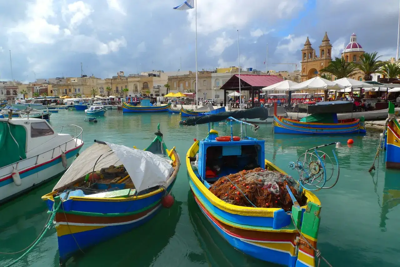 Kolorowe łodzie rybackie w Marsaxlokk, Malta. Ceny pamiątek i lokalnych produktów mogą być różne.