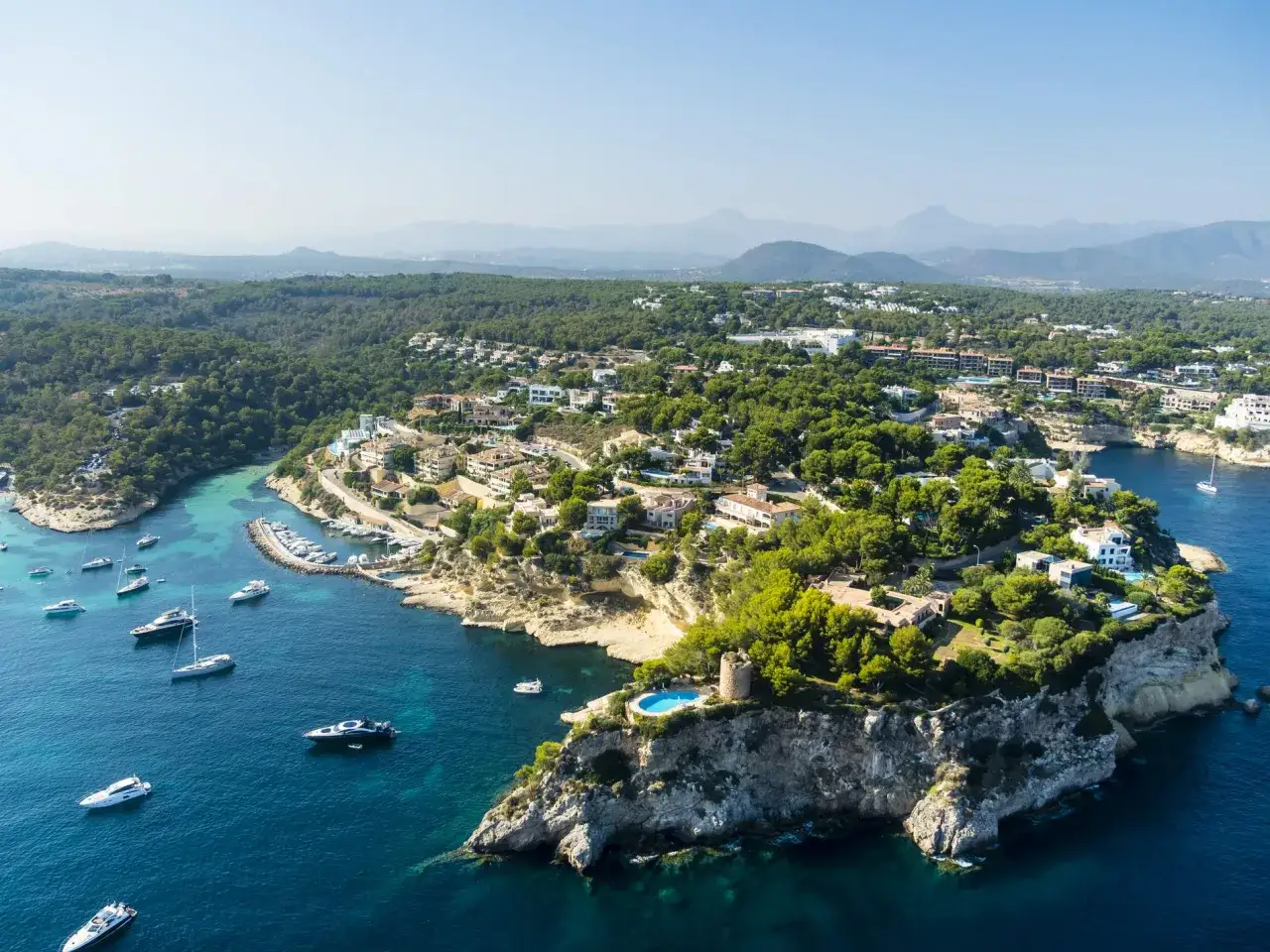 Malownicze wybrzeże Balearów, z luksusowymi willami, turkusową wodą i jachtami. Widok na skaliste klify z basenem i wieżą.