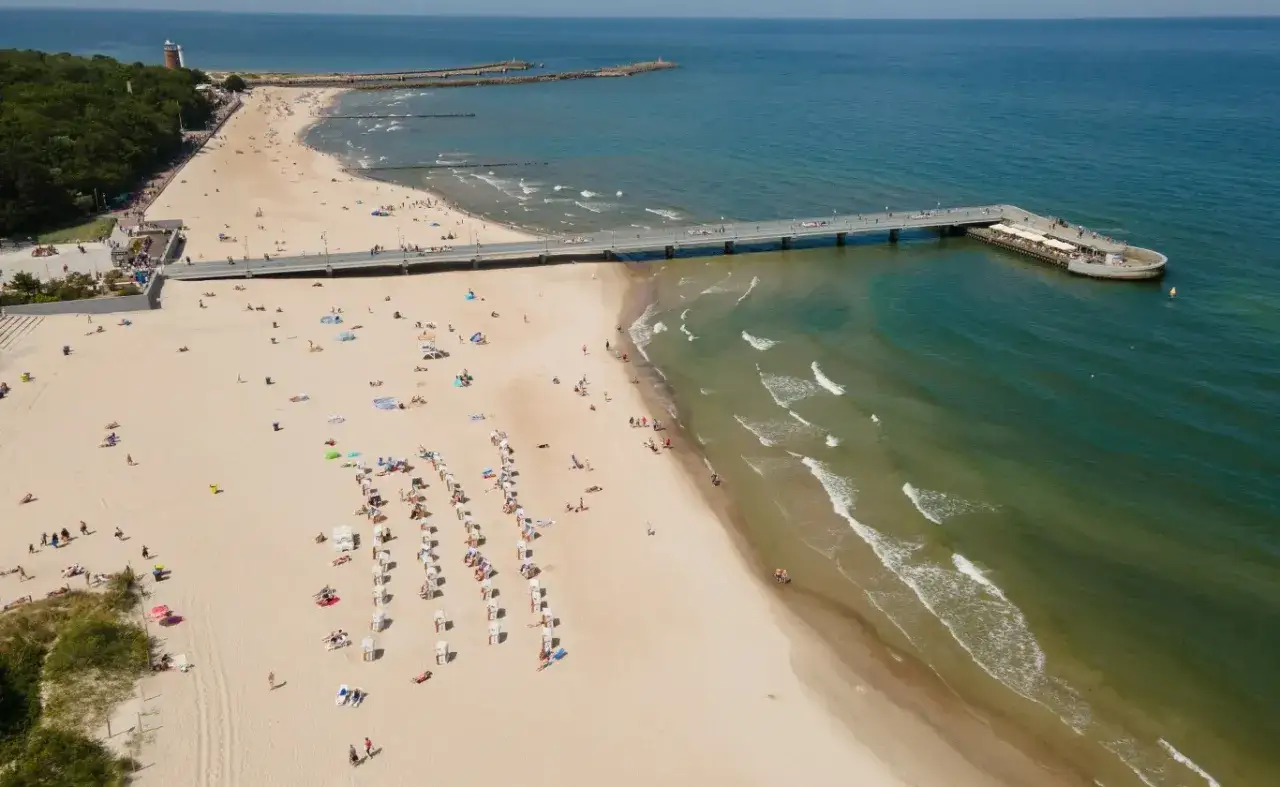 Plaża z molo, gdzie na majówkę przybyło wielu turystów. Słońce, piasek i szum fal zachęcają do wypoczynku.