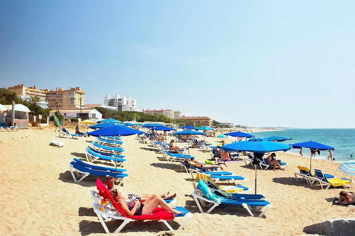 Słoneczny dzień na plaży w Malgrat de Mar. Leżaki i niebieskie parasole czekają na plażowiczów.