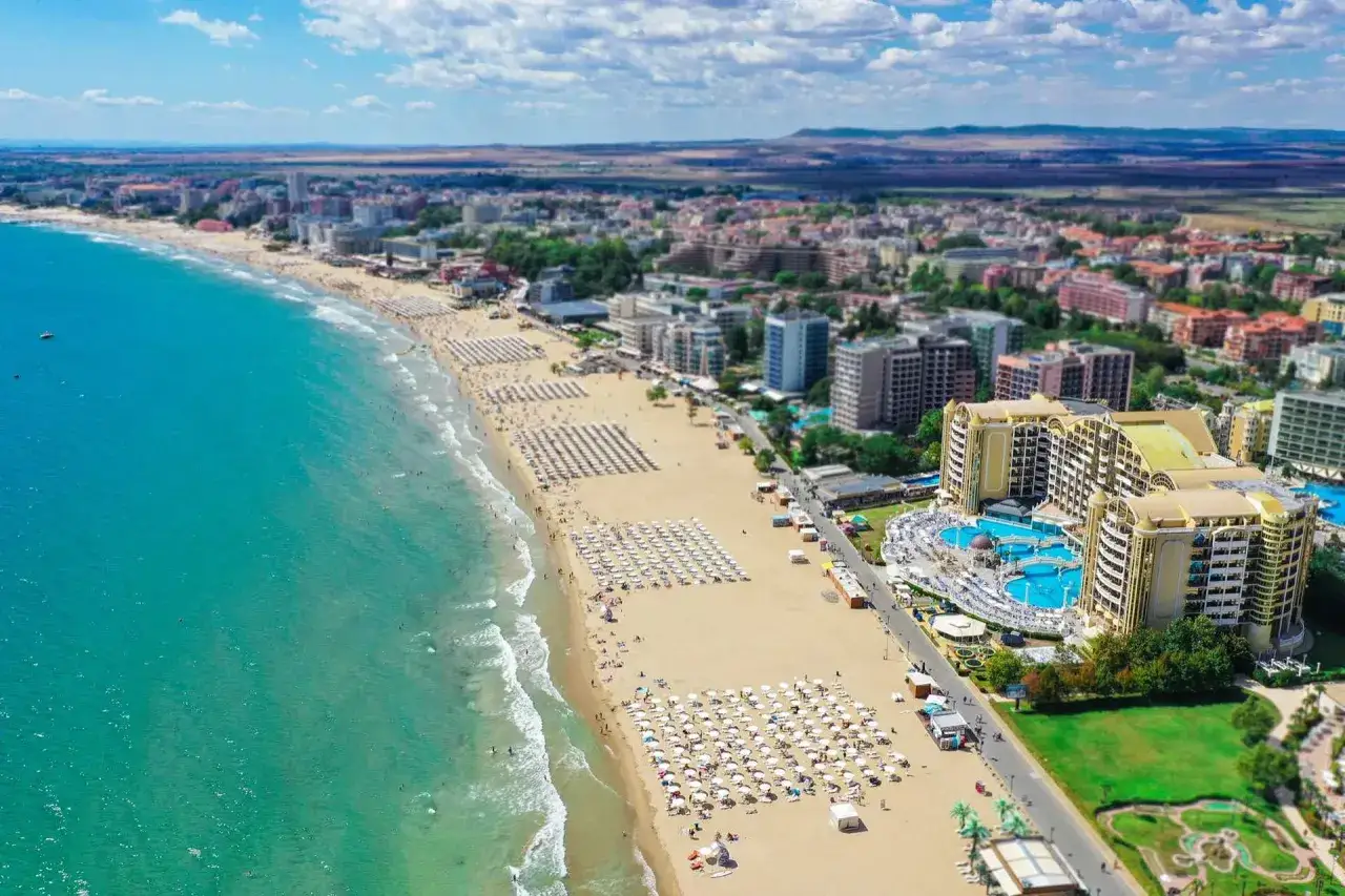 Słoneczny Brzeg, Bułgaria: rozległa plaża z białymi parasolami, turkusowe morze i luksusowy hotel z basenami.