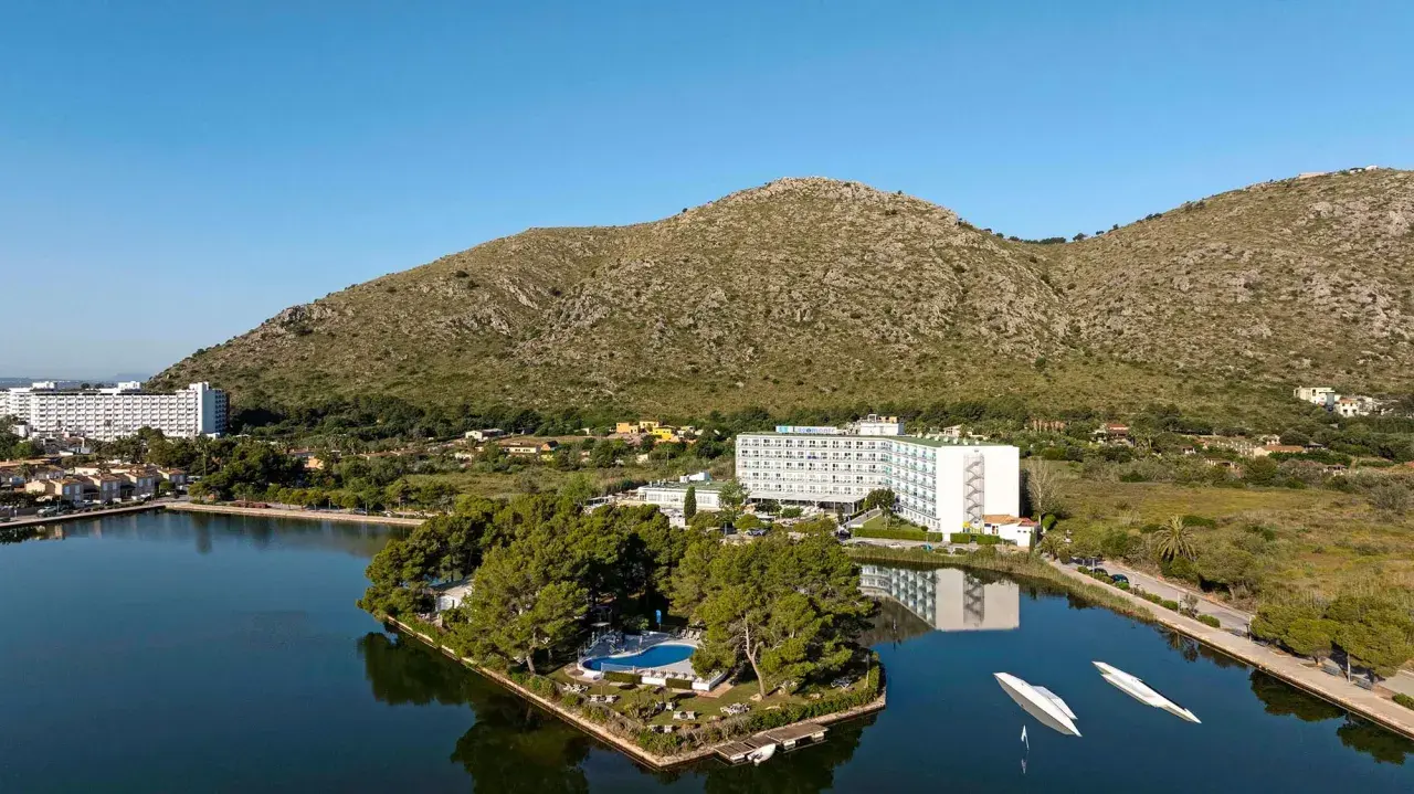 Hotel TUI Suneo Lagomonte z basenem na wyspie, otoczony jeziorem i górami.